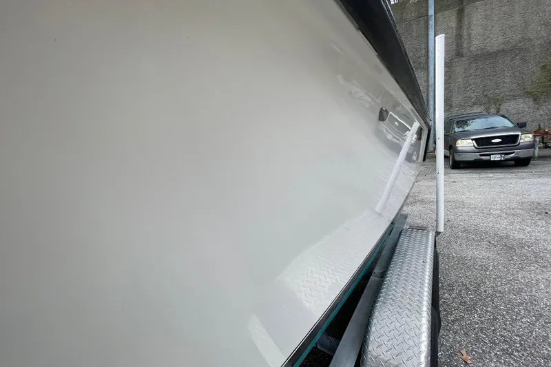 Slide: The Image of 1999 Contender 23 CC boat on trailer, side view with reflection, parked near a vehicle. - 8