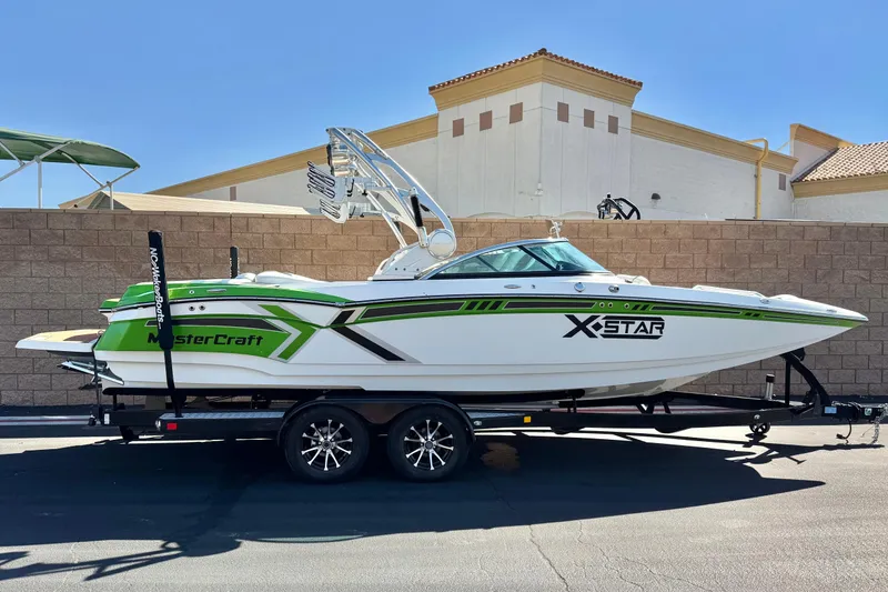 The Image of 2013 MasterCraft XStar boat on trailer, green and white design, parked outdoors. - 1