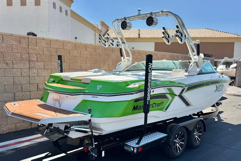 Slide: The Image of 2013 MasterCraft XStar boat with green accents on a trailer, parked outdoors. - 6