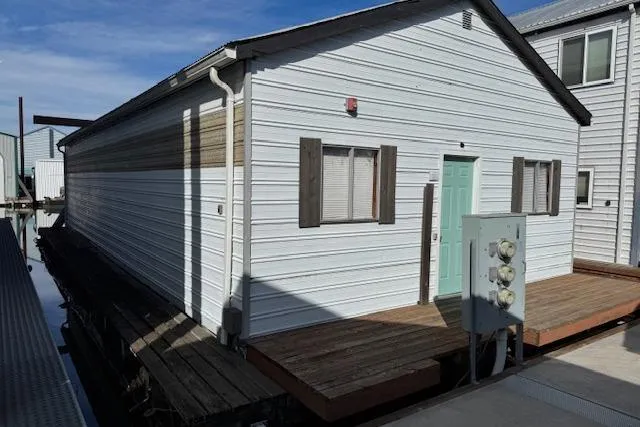 Slide: The Image of 1960 custom boathouse with white siding and teal door, docked on a sunny day. - 3