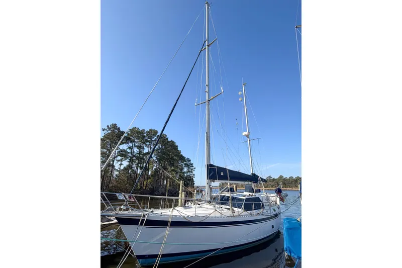 The Image of 1986 Nauticat 40 sailboat docked, featuring tall masts and blue canopy under clear sky. - 1