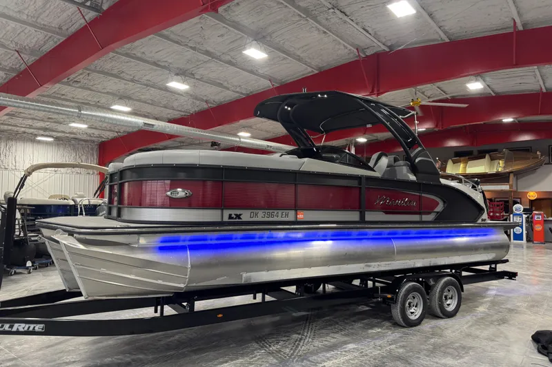 The Image of 2021 Manitou 25 LX pontoon boat with blue LED lights in a showroom. - 1