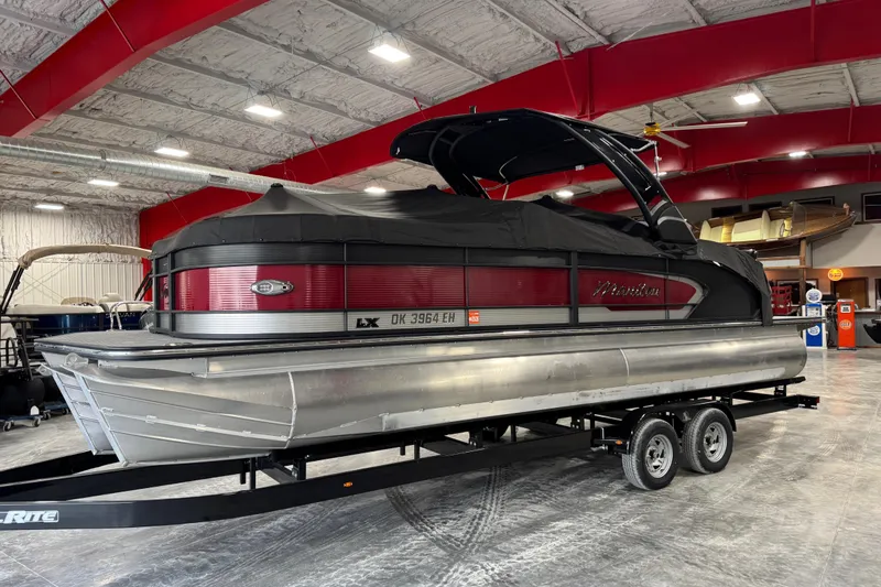 Slide: The Image of 2021 Manitou 25 LX pontoon boat in a showroom, covered and on a trailer. - 18