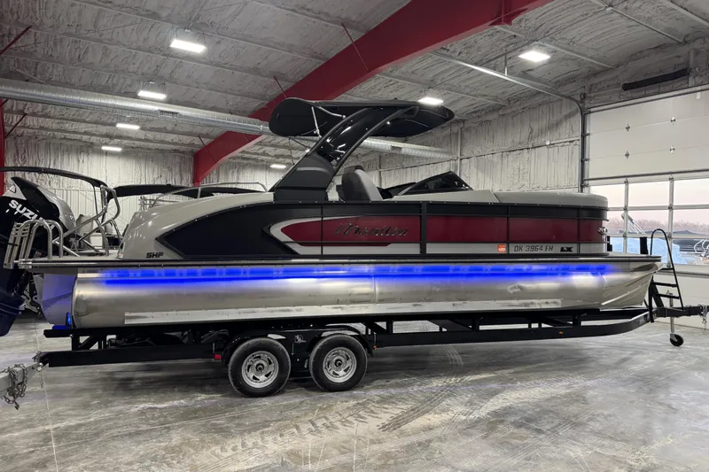 Slide: The Image of 2021 Manitou 25 LX pontoon boat with blue LED lights on trailer in a warehouse. - 4