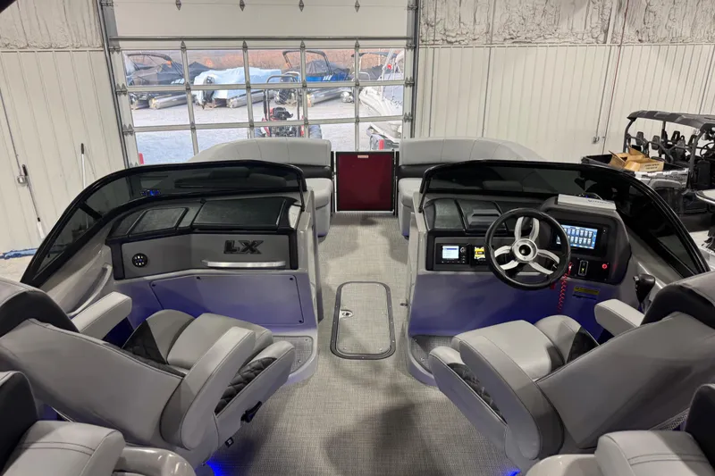 Slide: The Image of 2021 Manitou 25 LX boat interior with modern dashboard and seating in a garage setting. - 9
