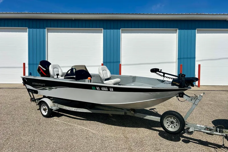 The Image of 2004 Starcraft D-Star 160 DLX SC boat on trailer, parked outside blue building. - 0
