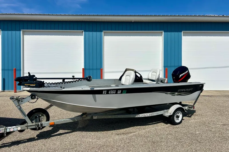 Slide: The Image of 2004 Starcraft D-Star 160 DLX SC boat on trailer, parked by blue storage units. - 2