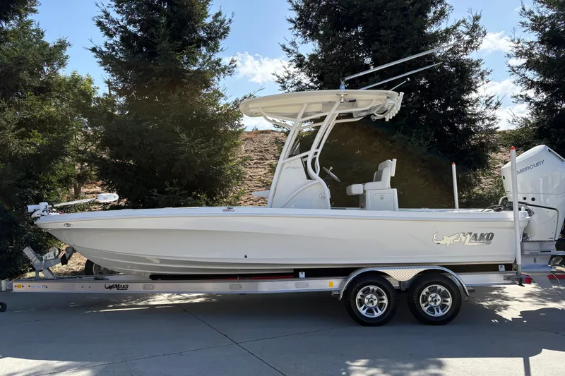 Slide: The Image of 2026 Mako 24 APEX boat on trailer, surrounded by trees, under clear sky. - 1
