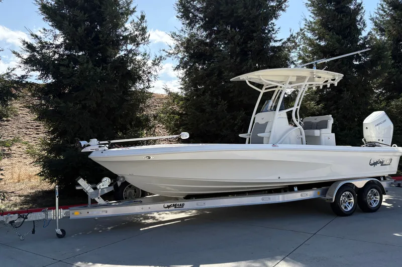 Slide: The Image of 2026 Mako 24 APEX boat on trailer, parked outdoors near trees. - 4