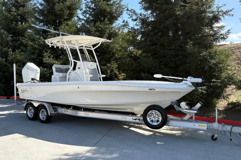 Slide: The Image of 2026 Mako 24 APEX boat on trailer, parked outdoors near trees. - 3
