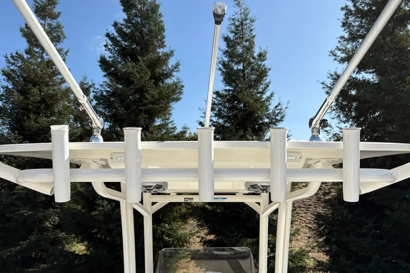 Slide: The Image of T-top rod holders on a 2026 Mako 24 APEX boat against a backdrop of trees. - 13