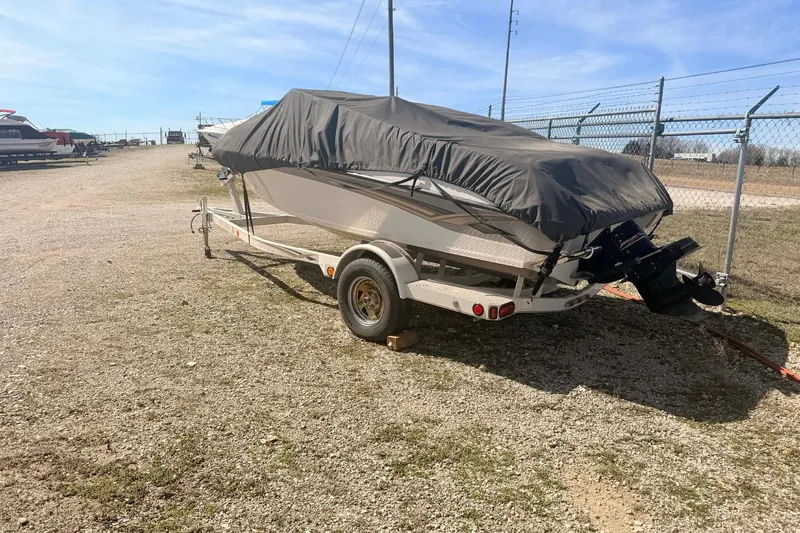 Slide: The Image of 2004 Crownline 180 BR boat on trailer, covered, parked outdoors near a fence. - 10