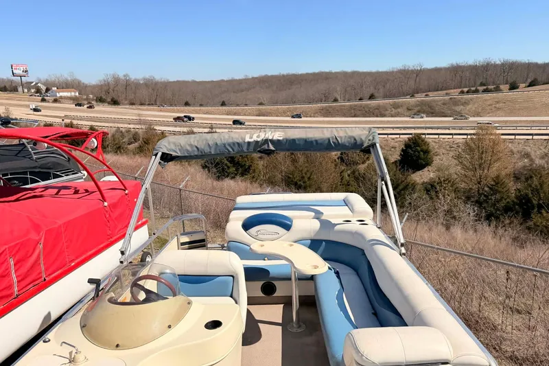 Slide: The Image of 2004 Lowe Jamaica 250 pontoon boat with blue and white seating, parked near a highway. - 12
