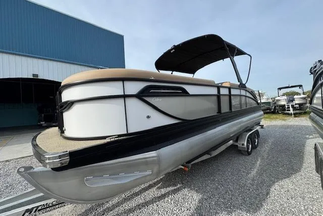 Slide: The Image of 2026 Barletta Cabrio 24M pontoon boat on trailer, parked near a blue building. - 3