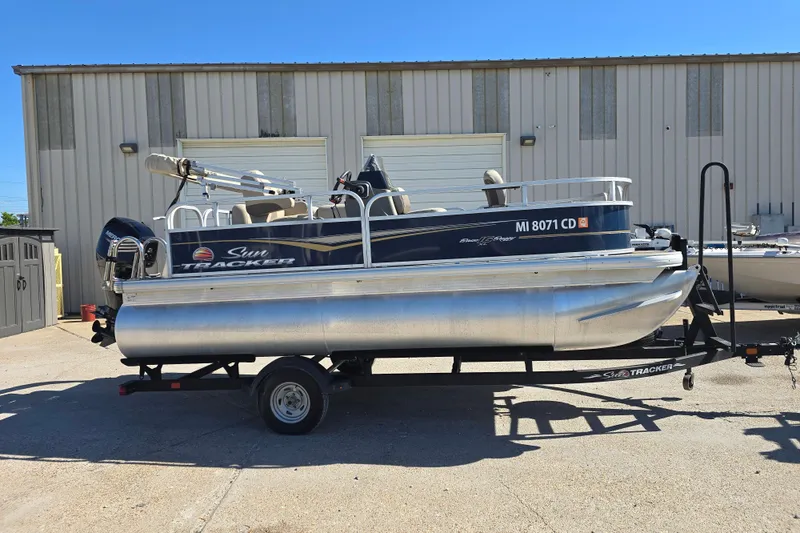 Slide: The Image of 2024 Sun Tracker Bass Buggy 16 XL Select pontoon boat on trailer, parked outdoors. - 5