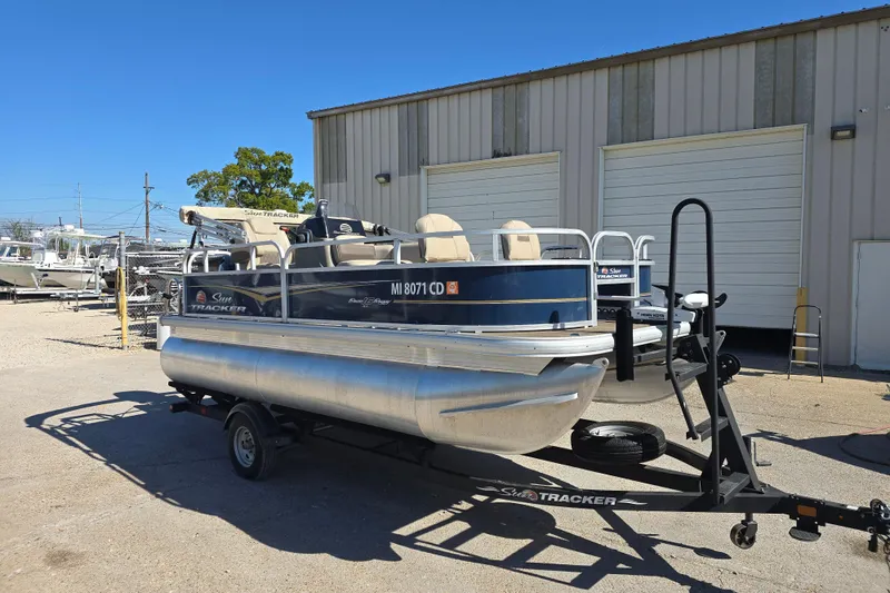 Slide: The Image of 2024 Sun Tracker Bass Buggy 16 XL Select pontoon boat on trailer outside warehouse. - 6