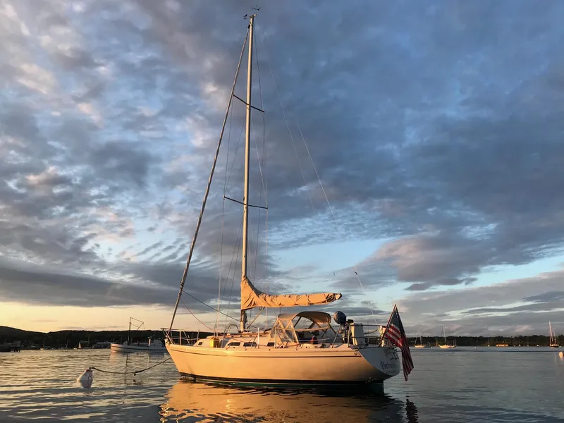 The Image of 1988 Ericson 34 sailboat anchored at sunset with an American flag. - 0