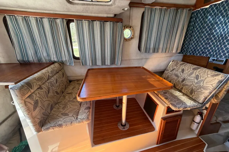 Slide: The Image of 2008 Ranger Tugs R-25 interior with wooden table, patterned cushions, and striped curtains. - 5