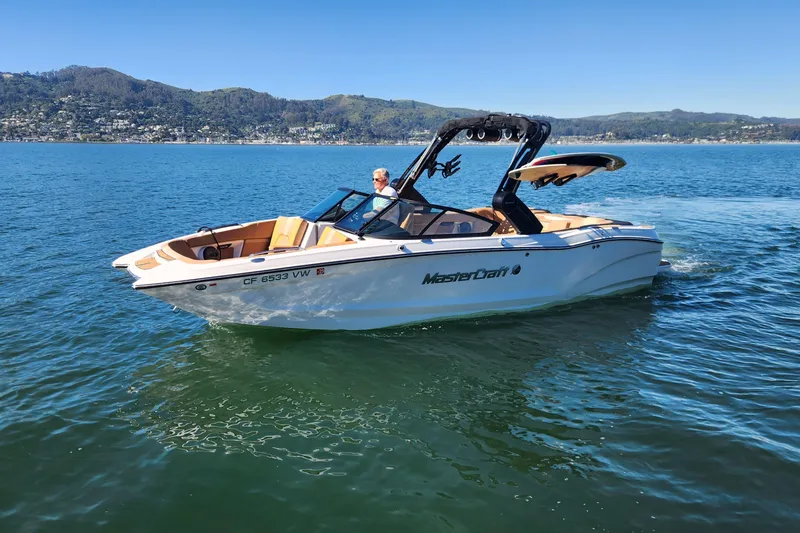 The Image of 2024 MasterCraft X24 boat cruising on a scenic lake with hills in the background. - 0