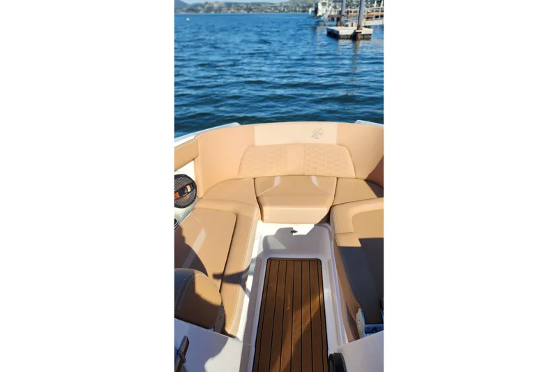 Slide: The Image of 2024 MasterCraft X24 boat interior with tan seating and wooden flooring on a sunny day. - 13