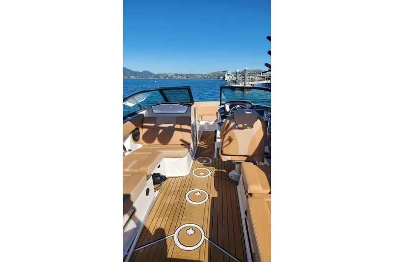 Slide: The Image of 2024 MasterCraft X24 boat interior with tan seating and wooden flooring on a sunny day. - 2