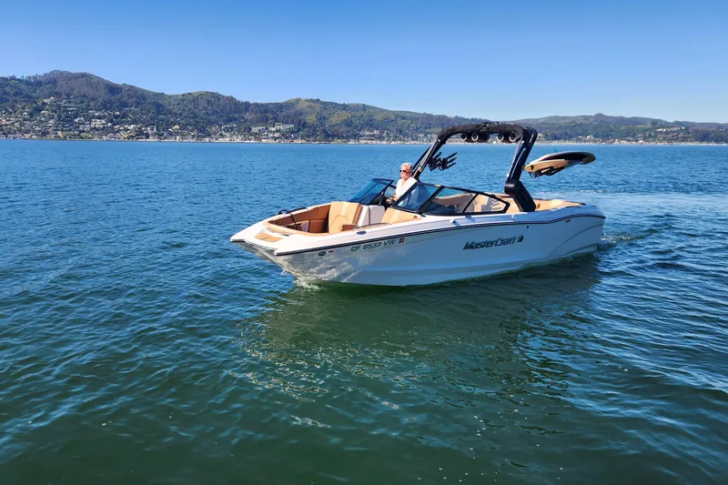 Slide: The Image of 2024 MasterCraft X24 boat cruising on a serene lake with scenic mountain backdrop. - 24