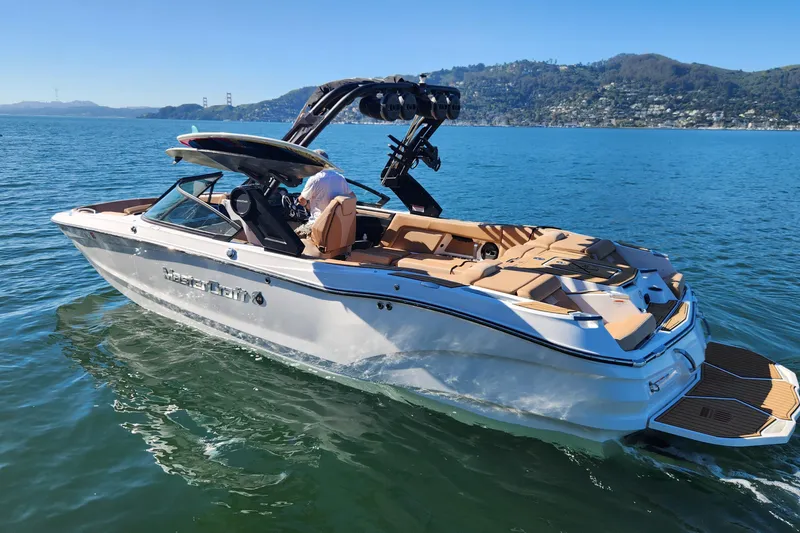Slide: The Image of 2024 MasterCraft X24 boat cruising on a sunny lake with scenic hills in the background. - 25