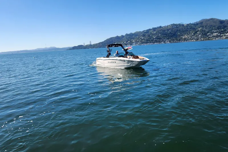 Slide: The Image of 2024 MasterCraft X24 boat cruising on a scenic lake with hills in the background. - 27