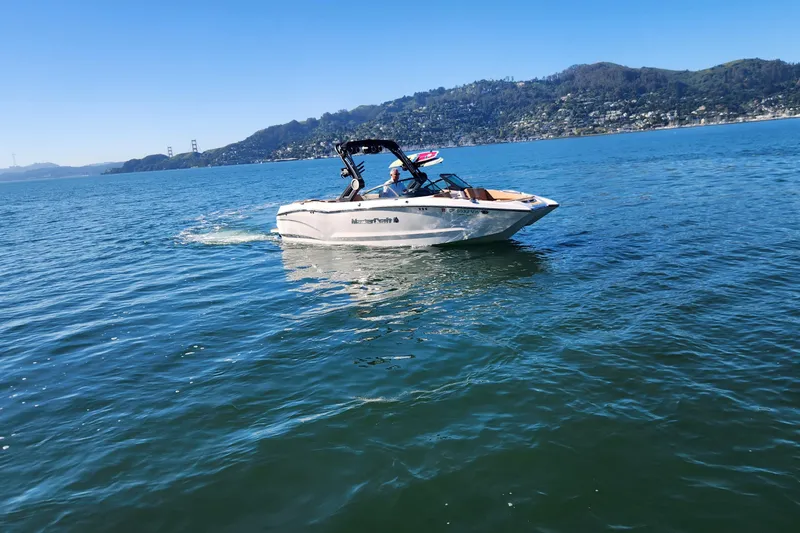 Slide: The Image of 2024 MasterCraft X24 boat cruising on a scenic lake with hills in the background. - 29