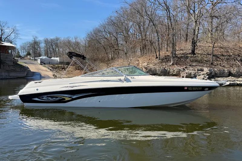 Slide: The Image of 2003 Rinker 282 Captiva Bowrider boat on calm water near a wooded shoreline. - 3