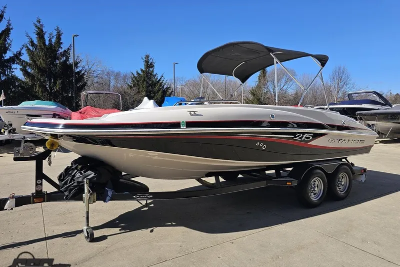 Slide: The Image of 2015 Tahoe 215 Xi boat on trailer, parked outdoors under clear blue sky. - 27