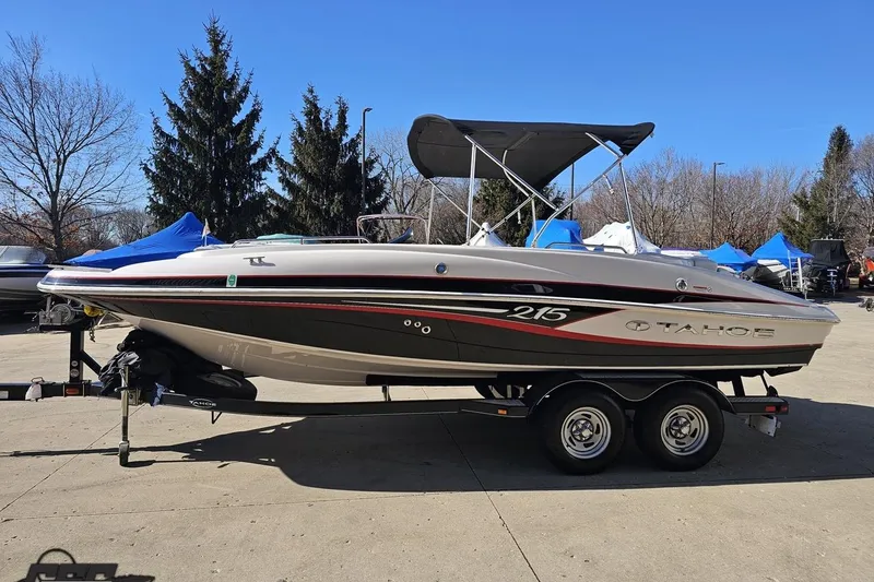 Slide: The Image of 2015 Tahoe 215 Xi boat on trailer, parked outdoors under clear blue sky. - 28