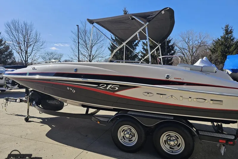 Slide: The Image of 2015 Tahoe 215 Xi boat on trailer, parked outdoors under clear blue sky. - 29