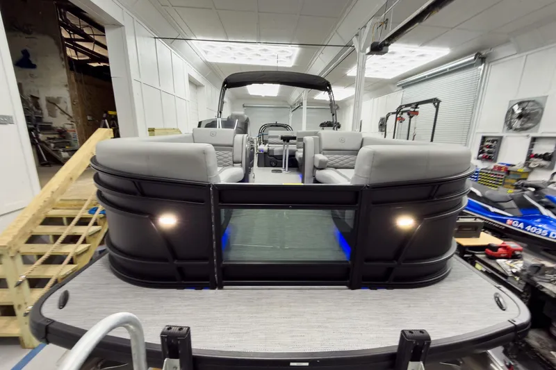 Slide: The Image of 2026 Godfrey Monaco 23' Tritoon with flip lounge, showcased in a modern indoor setting. - 12