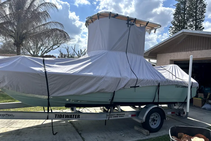Slide: The Image of 2020 Tidewater 1910 Bay Max boat covered on trailer, parked in driveway under cloudy sky. - 3