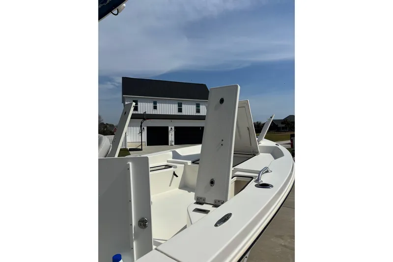 Slide: The Image of 2022 Bay Rider 239 Bay boat with open storage compartments, parked near a modern house. - 15
