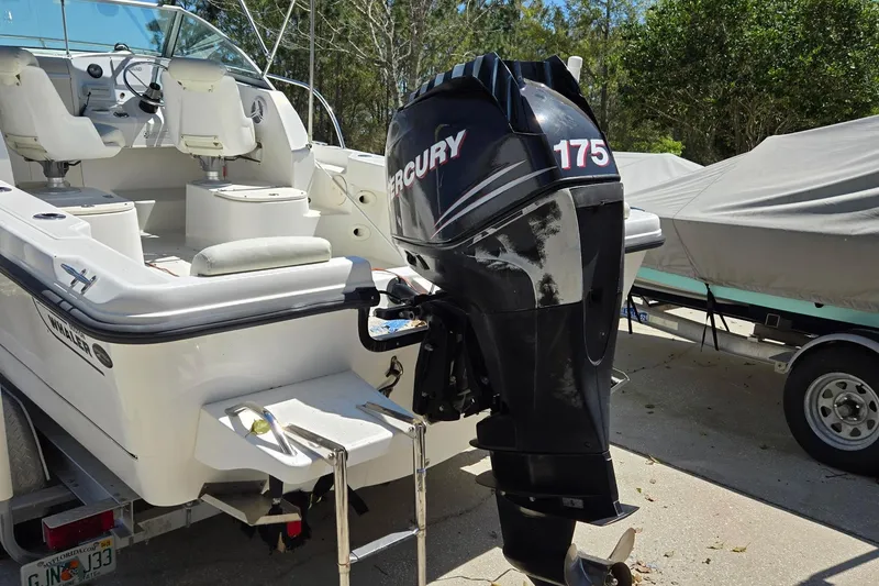 Slide: The Image of 2006 Boston Whaler 205 Conquest boat with outboard motor and ladder, parked outdoors. - 4