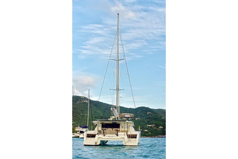 Slide: The Image of 2024 Fountaine Pajot Astrea 42 catamaran on serene water with lush hills in background. - 3