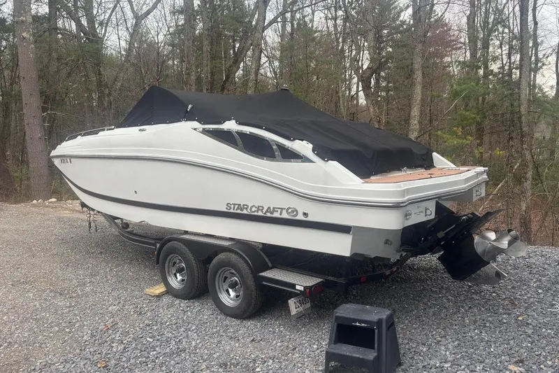 The Image of 2014 Starcraft Crossover 230 SCX IO boat on trailer, covered, in wooded area. - 1