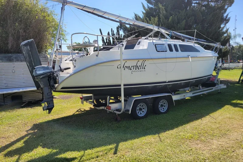 The Image of 2002 Hunter 260 sailboat on trailer with Yamaha outboard motor, parked on grass. - 0