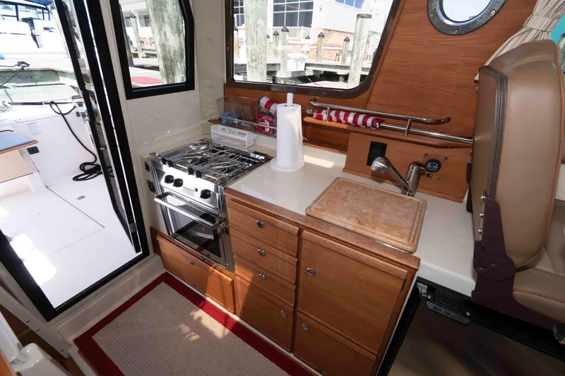 Slide: The Image of 2020 Ranger Tugs R-27 boat interior kitchen with stove, sink, and wooden cabinetry. - 7