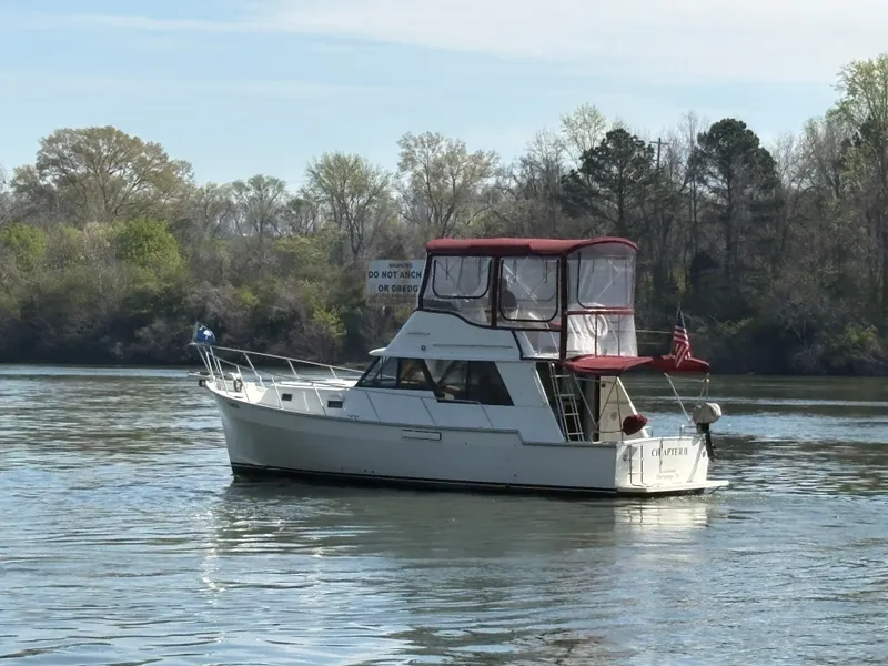 Slide: The Image of 1983 Mainship 34 Mark III on calm river with wooded backdrop. - 6