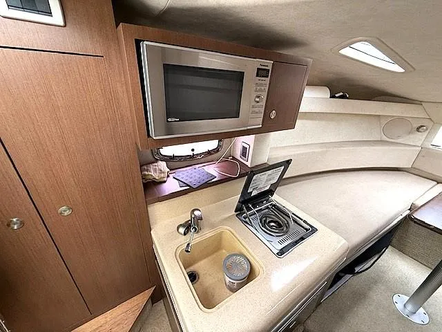 Slide: The Image of 2013 Sea Ray 260 Sundancer interior with kitchenette, featuring a microwave, sink, and stove. - 12
