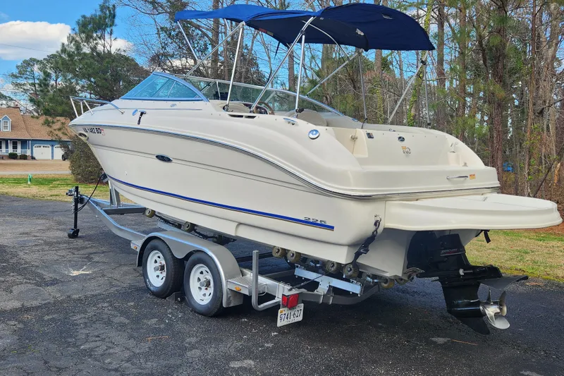 Slide: The Image of 2003 Sea Ray 225 Weekender boat on trailer, parked outdoors with trees in background. - 2