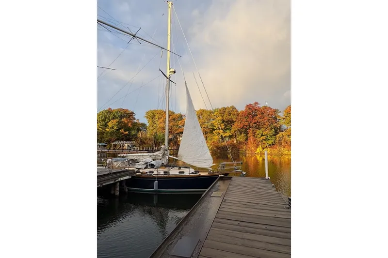 Slide: The Image of Sailboat Cape Dory 36, 1987 model, docked by autumn trees under a cloudy sky. - 13