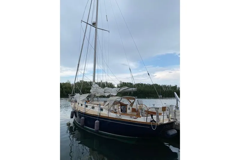 Slide: The Image of 1987 Cape Dory 36 sailboat docked on calm water under a cloudy sky. - 6