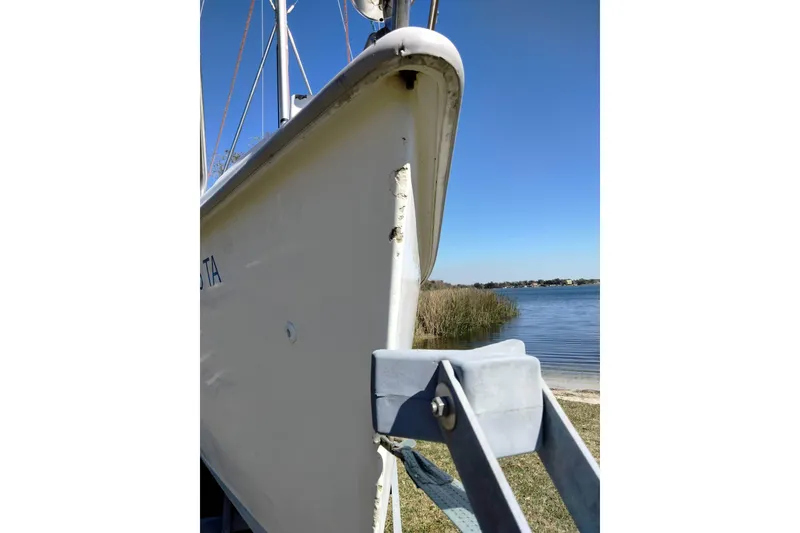 Slide: The Image of 1998 Hunter 240 sailboat bow with visible damage, near a calm lake. - 21