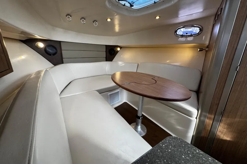 Slide: The Image of 2016 Boston Whaler 315 Conquest cabin interior with white seating and wooden table. - 50