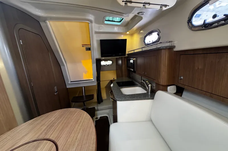 Slide: The Image of 2016 Boston Whaler 315 Conquest cabin interior with kitchenette, seating, and TV. - 54
