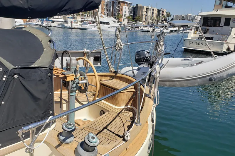 Slide: The Image of 1987 Hans Christian 33 sailboat docked in marina, featuring wooden deck and steering wheel. - 8
